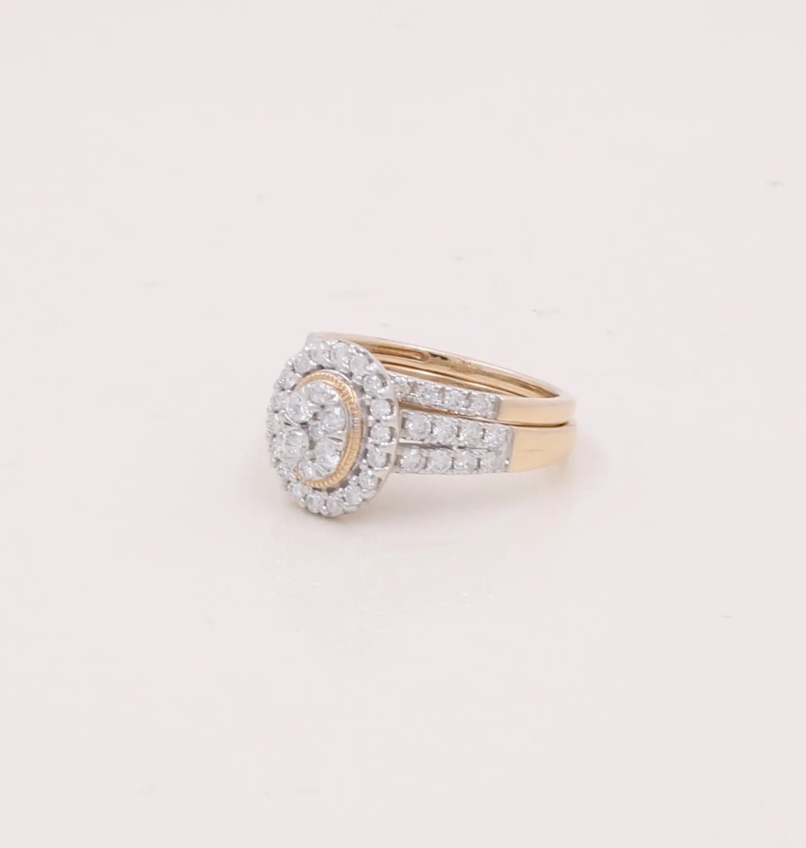 A stunning piece from our Miral Jewelry Collection, this 10K Yellow Gold Bridal Woman Ring features a gold band with a circular cluster of diamonds surrounded by a diamond halo, complemented by a double band embedded with diamonds.