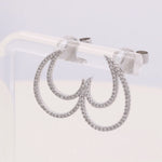 A pair of Miral Jewelry's 14K White Gold Fashion Diamond Women Earring Drops, adorned with small, sparkling clear stones, is displayed on a transparent stand, exuding the elegance of the Fashion Diamond collection.