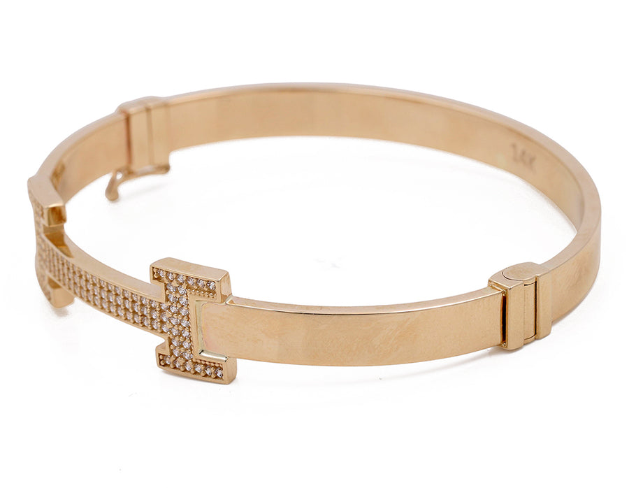 Miral Jewelry's 14K Yellow Gold Fashion Bracelet with Cubic Zirconias, featuring a clasp and a decorative element in the shape of a cross, on a white background.