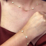 Close-up of a person wearing the Miral Jewelry 14K Yellow Gold Fashion Clover with Mother of Pearl Set, which includes a delicate necklace and bracelet, each adorned with small mother of pearl floral-shaped charms. They are dressed in a sleeveless maroon top.