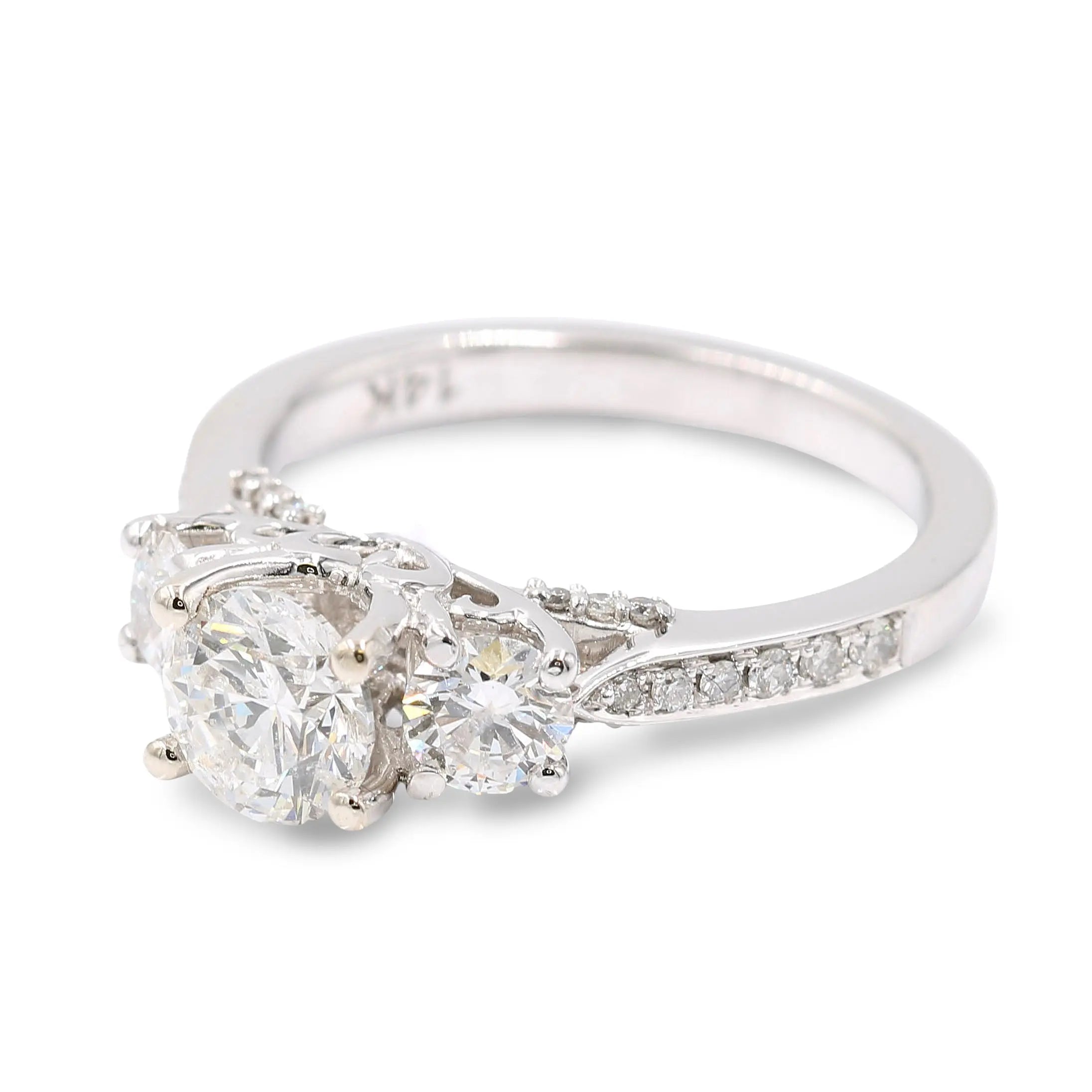 A stunning White 14 Karat 3 Stone Diamond Engagement Ring by Miral Jewelry featuring a larger center diamond flanked by two smaller hand-set diamond stones on a plain band. The 14 karat white gold band is adorned with small diamonds extending halfway around, making this an elegant choice for your special moment.
