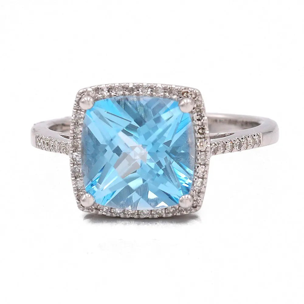 A Women's white 14 karat silver Contemporary Ring by Miral Jewelry featuring a large square-cut blue topaz surrounded by small round diamonds set in the band and around the central gem.