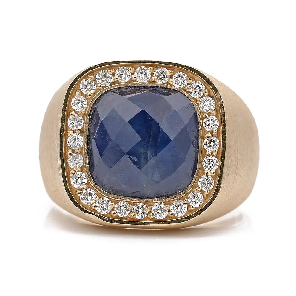 A Yellow Gold 14k Ring with Sapphire and Diamonds by Miral Jewelry, with a large sapphire in the center, surrounded by small white diamonds, set in a wide, smooth band.