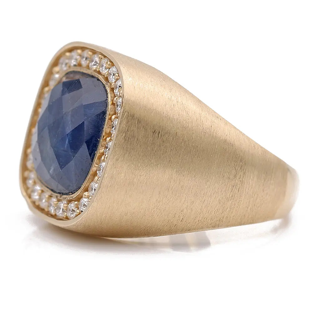 A Yellow Gold 14k Ring with Sapphire and Diamonds by Miral Jewelry featuring a large, faceted sapphire surrounded by small white diamonds.