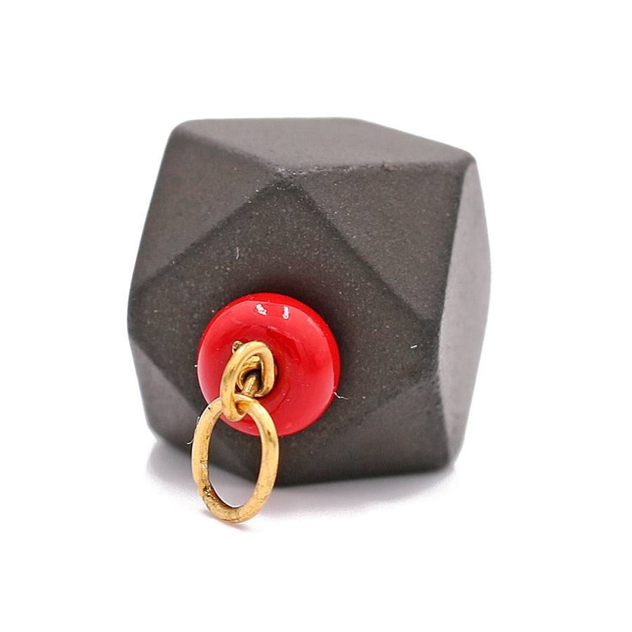 A Miral Jewelry 14k Yellow Gold Azabache pendant featuring a black and red geometric cube with a gold ring attached to it, providing protection.