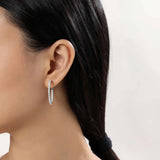 Close-up of a person's ear adorned with large, textured inside-out Hoop Earrings by Miral Jewelry, crafted from sterling silver, their dark hair tied back in a low ponytail.
